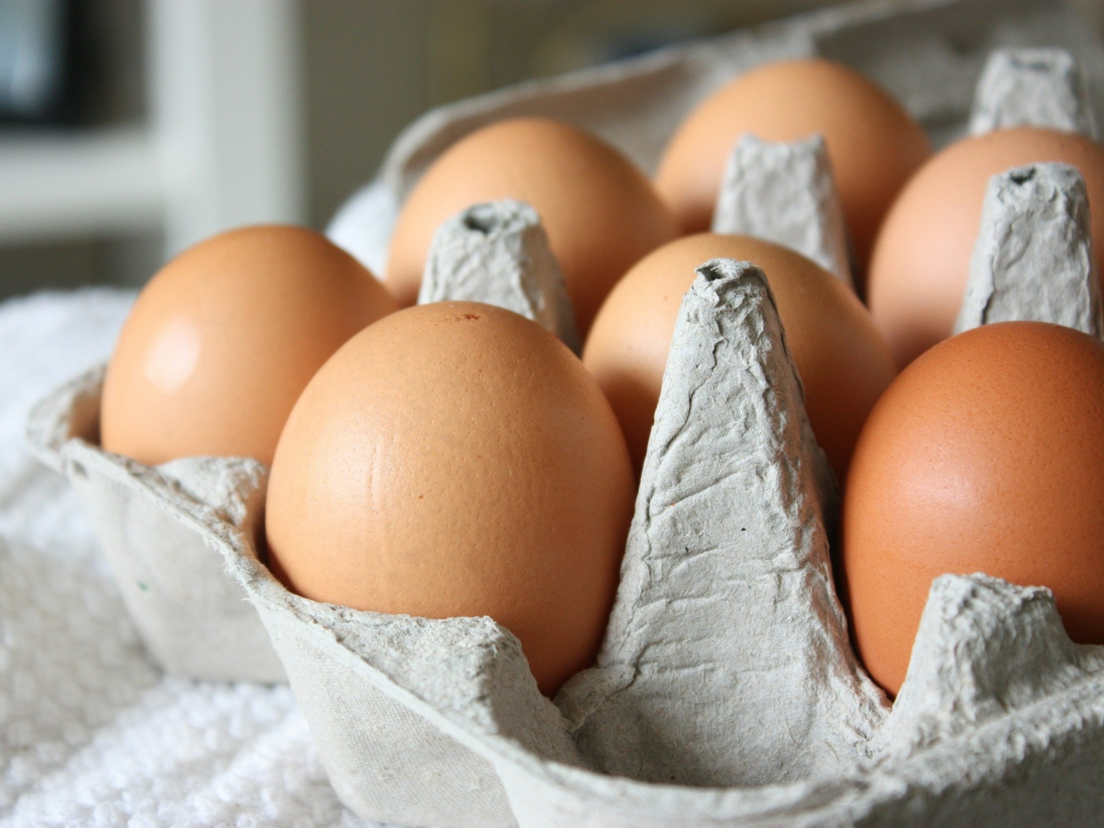 Rhode+Island+Red+Chicken+Egg Fresh farm eggs in a carton featuring various colors, including brown, white, and cream, resting on a rustic wooden surface. Ideal for cooking and baking.